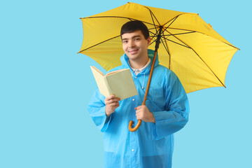 Poster - Young man in raincoat with umbrella reading book on blue background