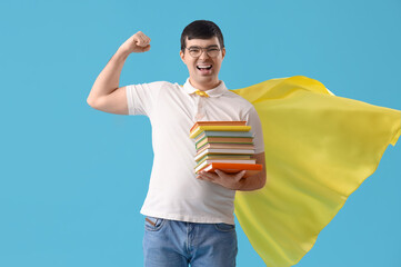 Wall Mural - Young man in superhero cape with books showing muscles on blue background