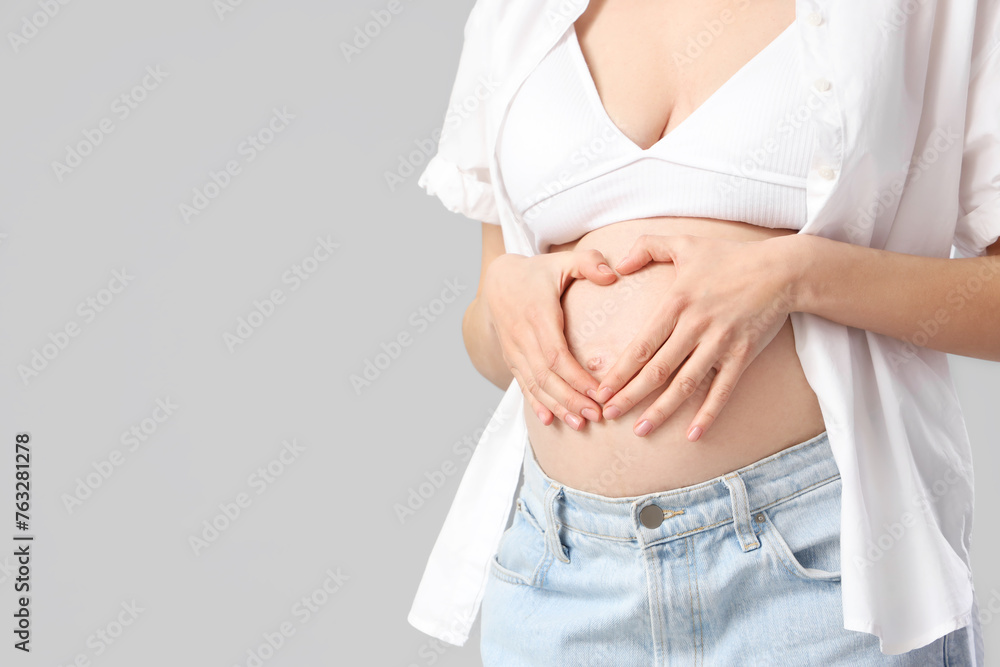 Young pregnant woman making heart gesture on light background, closeup