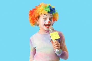 Wall Mural - Funny little girl in clown wig with microphone on blue background. April Fools' Day celebration