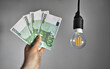 Man holds money next to a light bulb. Expensive electricity concept.