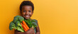 A studio shot of a smiling African boy holding fresh broccoli and carrots on a yellow background. Copying the space. The concept of healthy baby food.