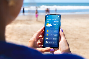 woman outdoors on the beach checking the weather forecast on an app on her mobile phone.