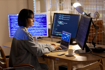 Wall Mural - female programmer with laptop and computer monitors working in office at night