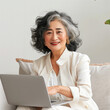 older Asian woman working on laptop computer, sitting on a couch smiling