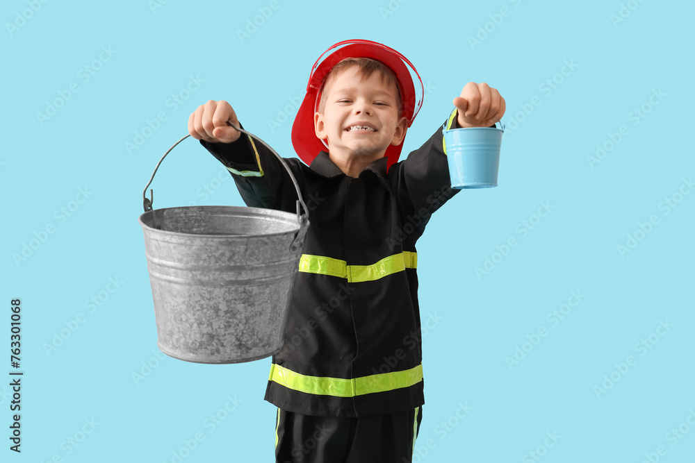 Cute little firefighter with buckets on blue background