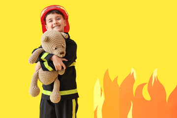 Poster - Cute little firefighter saving toy bear from paper flame on yellow background