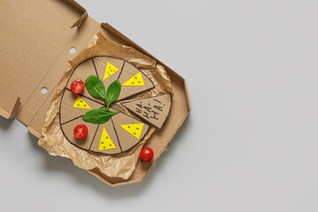 Wall Mural - Carton pizza with tomatoes and basil on white background. April Fools Day prank