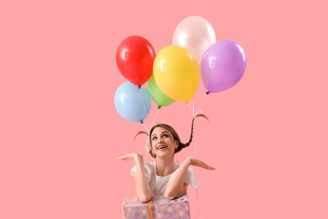 Wall Mural - Young woman with balloons and gift box on pink background