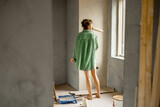 Fototapeta Przestrzenne - Young woman paints walls while making repairment of a new house. Creative process of home renovation and repair concept