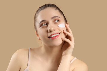 Wall Mural - Young woman with facial cream on beige background, closeup