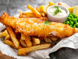 Fototapeta Natura - A view of a classic British fish and chips meal, featuring a large piece of golden, crispy battered fish alongside a generous portion of thick-cut fries.
