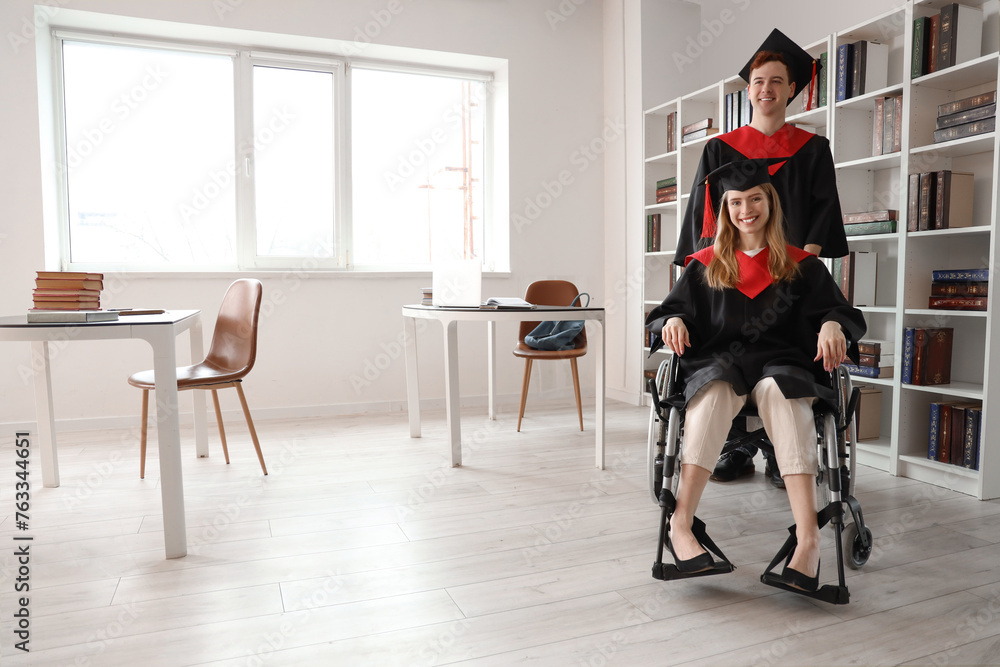 Female graduate in wheelchair with her classmate at university