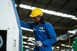 © KANGWANS - A man in a blue work suit is fixing a machine. He is wearing a yellow hard hat and gloves