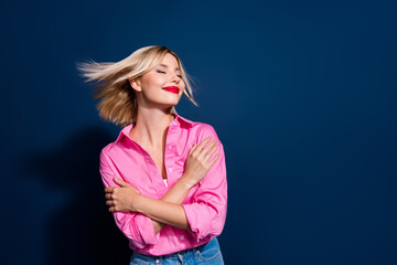 Poster - Photo portrait of pretty young girl hug self shoulders fluttering hair wear trendy pink outfit isolated on dark blue color background