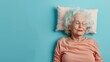 Elderly woman sleeping on pillow isolated on pastel blue colored background Sleep deeply peacefully rest. Top above high angle view photo portrait of satisfied .senior wear pink shirt