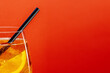 Detail of aperol spritz aperitif with orange slice, ice cubes and black drinking straw on bright red background with space for text.