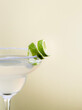 Close up of lime zest on salt rim of margarita cup glass isolated on pale pale yellow pastel color background with room for text.