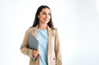 Positive indian or arabian brunette business woman, dressed in elegant suit, manager, designer, holding laptop while standing on isolated white background, looking away and smiling