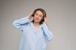 Enjoying the music with eyes closed.  blonde woman in blue shirt touching her black headphones on her neck. Gray background studio shot 
