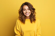 Portrait of a smiling young woman over yellow background. Young woman cute face expression posing in yellow hoodie on yellow background.