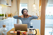 © Davor - Woman holding neck at kitchen table with laptop at home