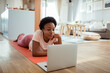 © Davor - Woman on yoga mat looking at laptop in living room