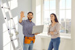 © Studio Romantic - Worker talking to young woman about repairs and renovations at her home. Smiling man together with homeowner girl standing in light room by step ladder, holding laptop PC, and pointing at some changes