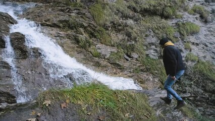 Wall Mural - Man traveler walks Hiking route in the Alps and enjoys the view of a mountain river and waterfall. Incredibly beautiful views in the Alpine mountains.