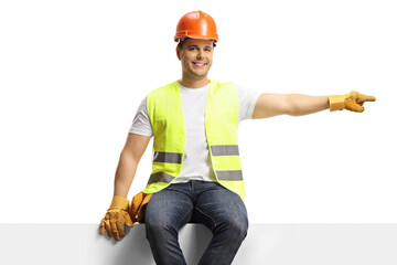 Wall Mural - Construction worker sitting on a blank panel and pointing to the side