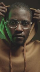 Wall Mural - vertical chest up portrait of young serious black male programmer pulling up hood and looking at cam