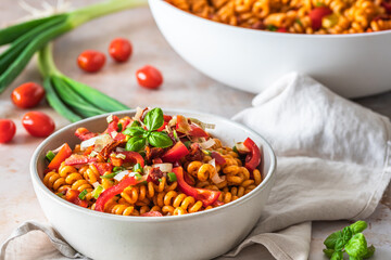 Pasta salad with red pepper, tomatoes, spring onions and basil in a white bowl