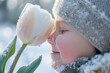 Cute spring image of a child closeup smelling a tulip flower, still covered with snow