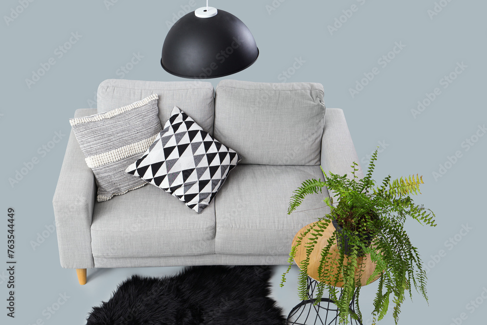 Modern living room interior with sofa, pillows and flowerpot on grey background