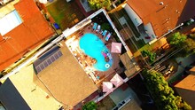 Aerial Top Shot Of People Enjoying Pool Party Outside Houses In City, Drone Flying Upwards On Sunny Day - Culver City, California
