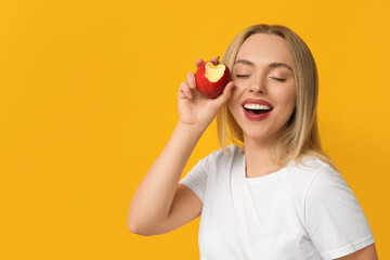 Wall Mural - Young woman eating apple on yellow background, closeup