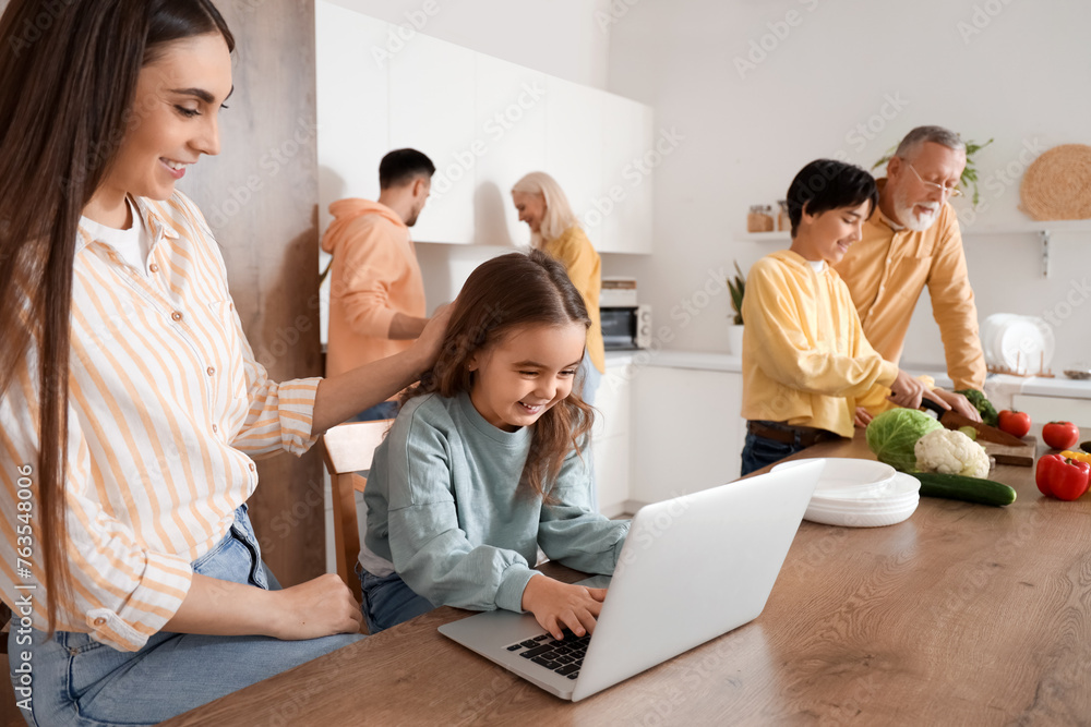 Little girl using laptop and her family in kitchen
