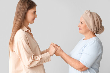 Sticker - Mature woman after chemotherapy with her daughter holding hands on light background. Stomach cancer concept