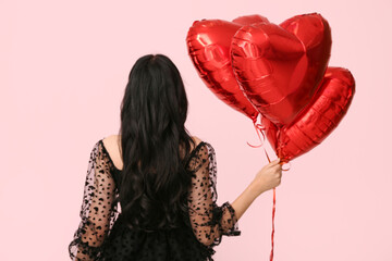 Canvas Print - Beautiful young woman with dark wavy hair in black dress holding balloons on pink background, back view