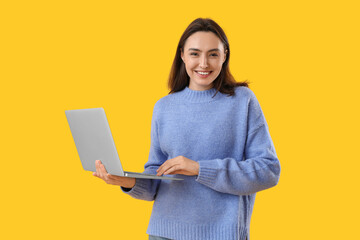 Pretty young woman working with laptop on yellow background