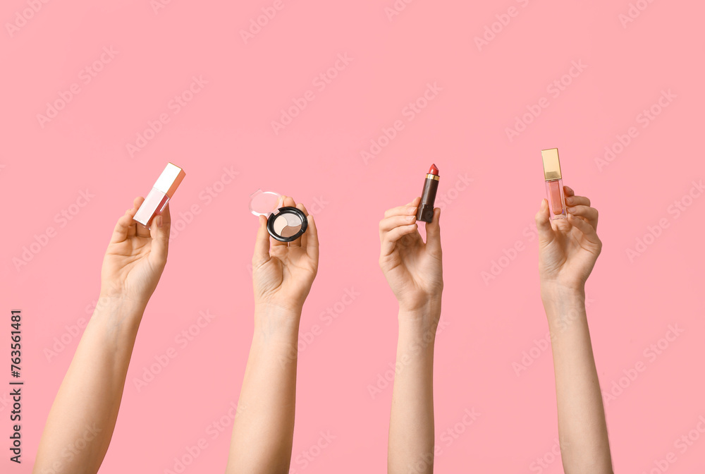 Female hands with eyeshadows palette, lip glosses and lipstick on pink background