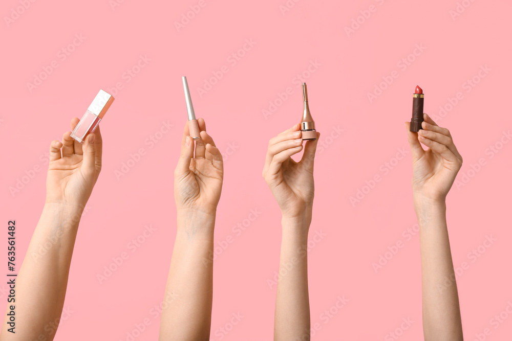 Female hands with lipstick, lip gloss and eyeliners on pink background
