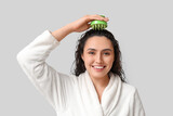 Fototapeta Mapy - Beautiful young woman using hair scalp massager on grey background