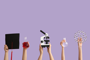 Female hands holding molecular model with filled flasks, microscope and graduation hat on lilac background. Chemistry lesson concept