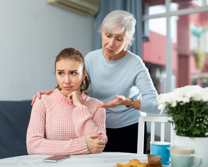 Wall Mural - Careful loving elderly mother comforting her upset adult daughter at home table.