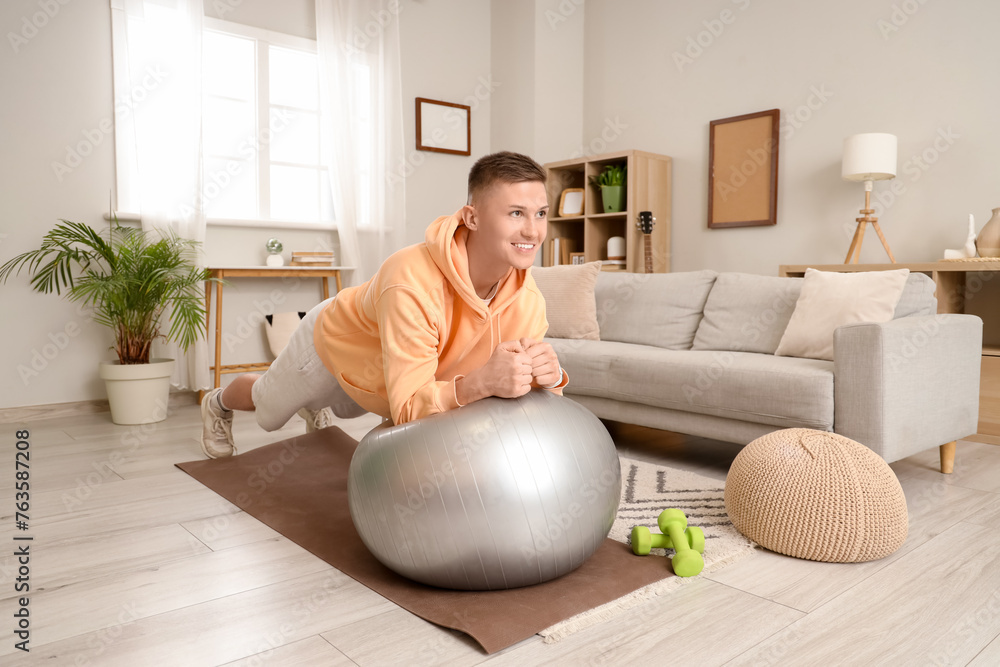 Sporty young man training with fitball at home