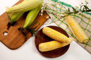 Clay plate with two cobs sweet corn on white wooden background..