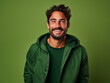 Hombre latino, joven, atractivo y con barba corta, feliz, usando ropa casual de color verde posando sobre un fondo del mismo color