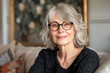 Smiling middle aged mature grey haired woman looking at camera happy old lady in glasses posing at home indoor positive single senior retired female sitting on sofa in living room headshot portrait