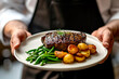 A chef is holding a plate of food with a steak and potatoes